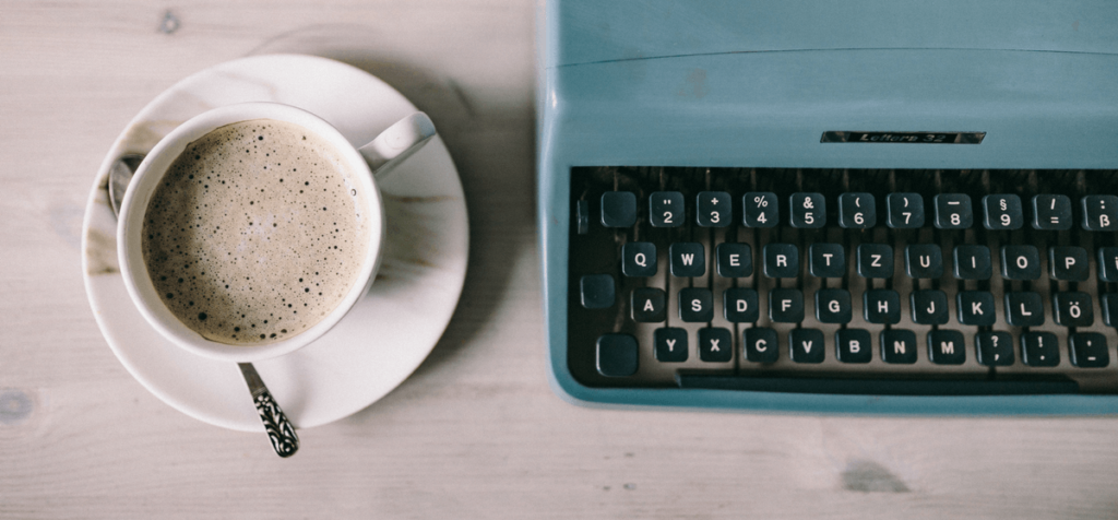 weißer Holztisch mit einer Tasse Kaffee und Schreibmaschine