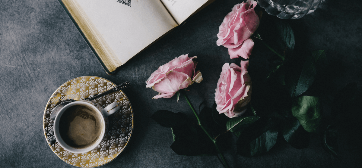Kaffeetasse, rosa Rosen und geöffnetes Buch auf dunklem Hintergrund
