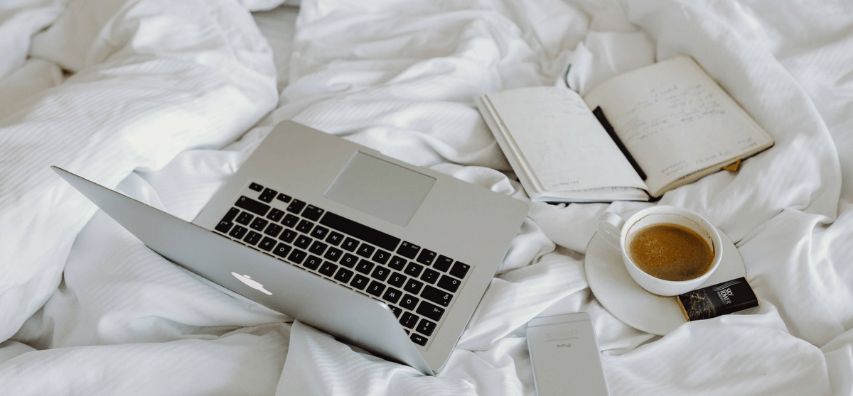 MacBook, Kalender, Kaffee und Smartphone liegen auf einem Bett