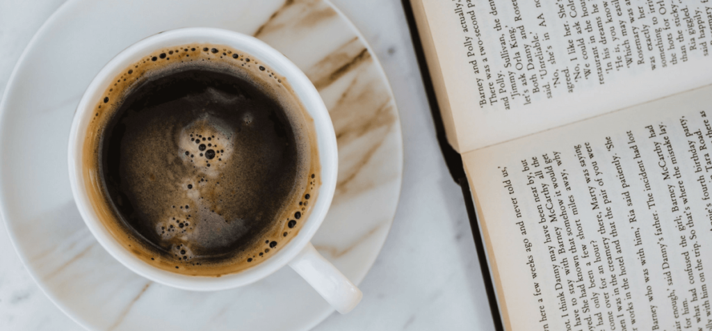 Kaffeetasse und geöffentes Buch liegen auf Marmortisch