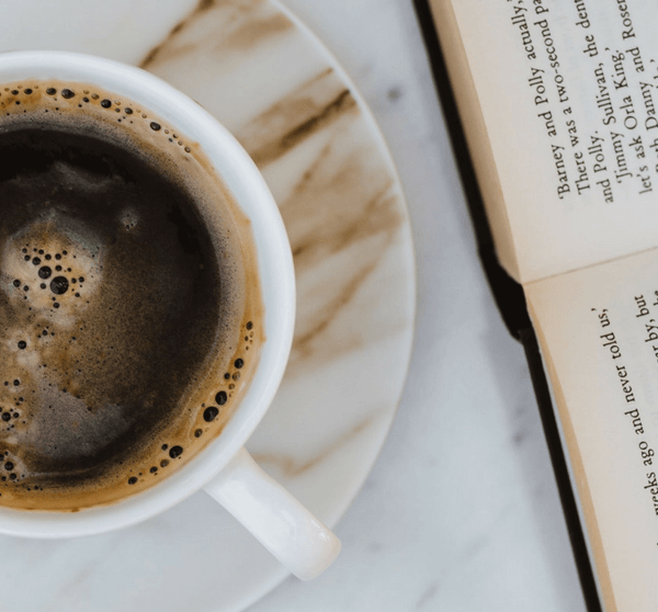 Kaffeetasse und geöffentes Buch liegen auf Marmortisch